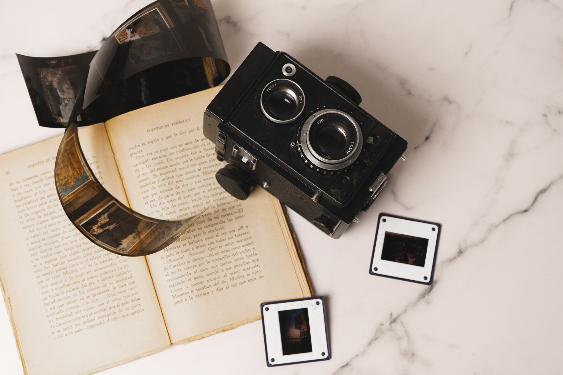 Camera, Film Negative and Book on Marble Background